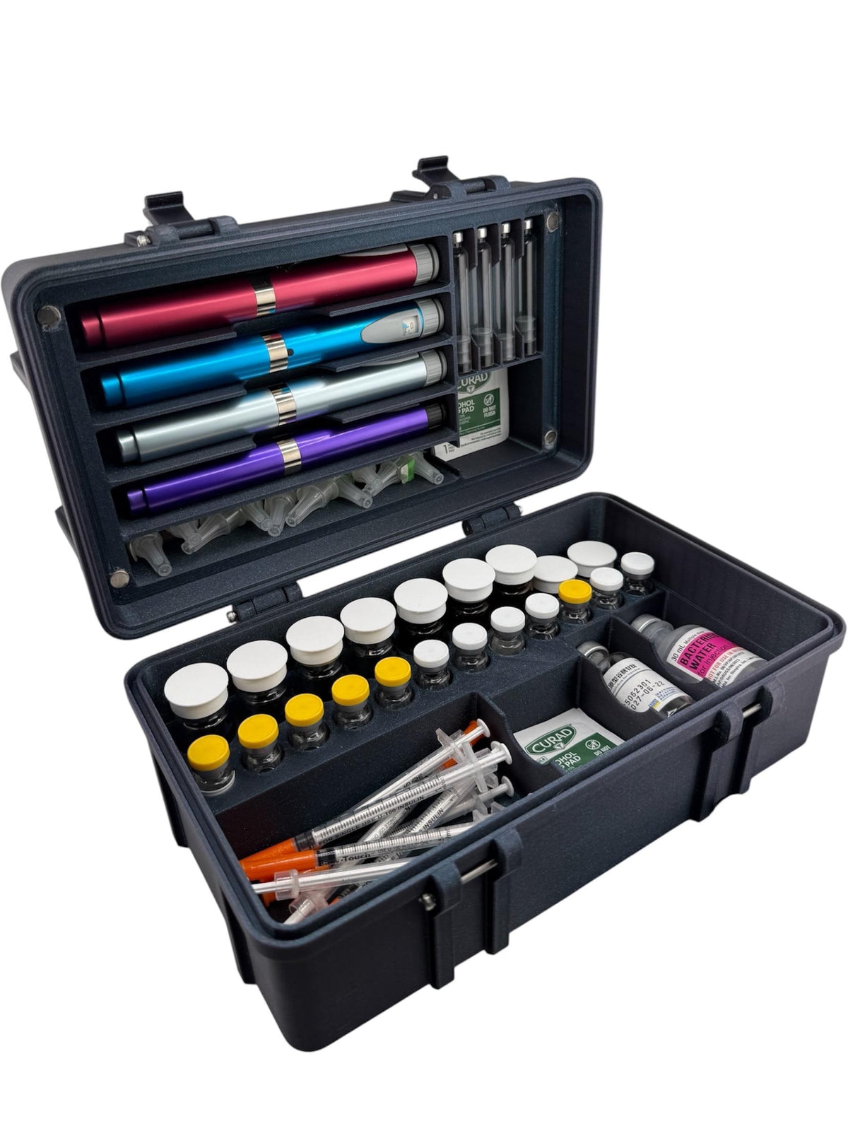 May include: A dark gray, rectangular, hard-shell carrying case with a hinged lid, containing four colored injection pens, multiple small glass vials with white and yellow caps, several clear syringes with orange caps, and Curad alcohol prep pads
